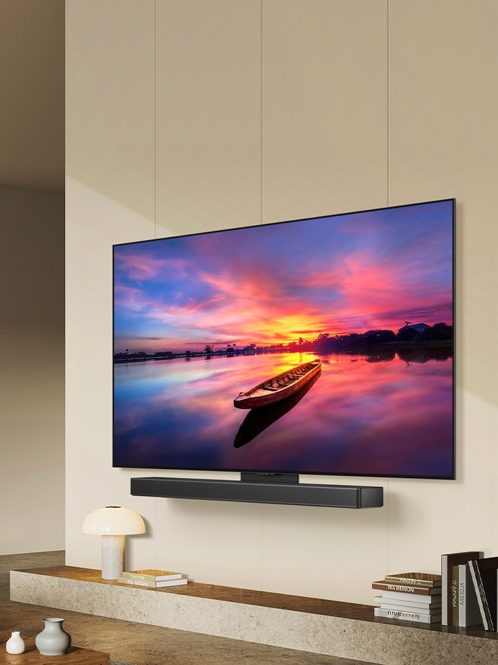 Der LG OLED evo TV C4, 45 Grad nach links geneigt, zeigt einen wundersch?nen Sonnenuntergang mit einem Boot auf einem See. Der Fernseher ist über das Matching-Kit an einer LG Soundbar in einem minimalistischen Wohnraum befestigt.	