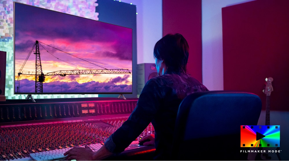 Ein Filmregisseur blickt auf einen gro?en TV-Monitor und bearbeitet etwas. Der Fernsehbildschirm zeigt einen Kran vor einem violetten Himmel. Das Logo des FILMMAKER MODE befindet sich in der unteren rechten Ecke.