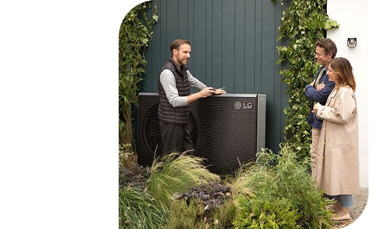 Ein Ingenieur steht neben der neuen schwarzen THERMA V und spricht mit einem jungen Paar, w?hrend er die Luft-Wasser-W?rmepumpe von LG installiert.