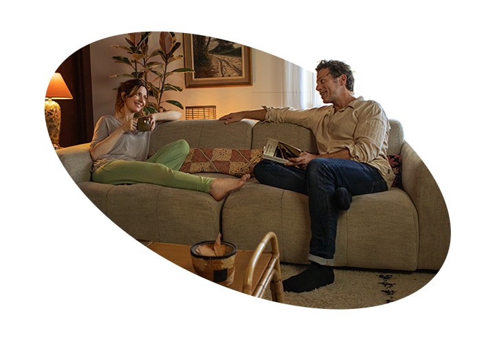 Eine Frau und ein Mann sitzen auf einer Couch im Haus und unterhalten sich l?chelnd. Neben dem Bild ist ein Quiet Mark-Zertifizierungslogo zu sehen.