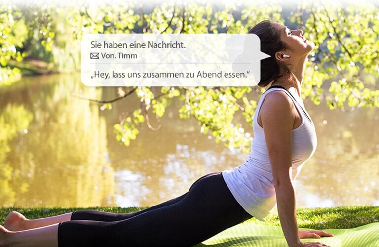 Eine Frau dehnt sich und beugt sich nach unten, um den Boden zu berühren, w?hrend sie sich eine von ihren Ohrh?rern vorgelesene Nachricht anh?rt.