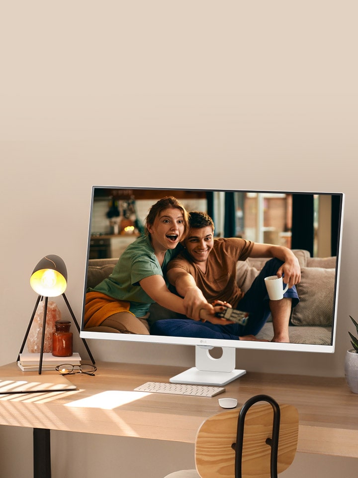 Auf dem Schreibtisch am sonnenbeschienenen Fenster steht ein intelligenter Monitor, auf dessen Bildschirm ein Film zu sehen ist. Neben dem Monitor befinden sich eine Lampe und eine Topfpflanze. Auf dem Schreibtisch befinden sich eine Tastatur und eine Maus.