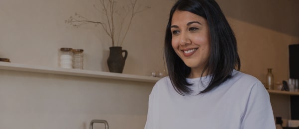 Frau gie?t Tee in eine Teekanne in einer modernen Küche und l?chelt entspannt.