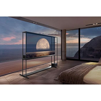 LG SIGNATURE OLED T displays a moon depicted above a shore on the transparent screen. The LG SIGNATURE OLED T sits in the middle of a room with a cliff side view that looks out to the sea. On the right is a bed and a lounge chair. 
