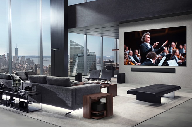 Stue med et LG True Wireless TV og en LG Soundbar, som er v?gmonteret. Zero Connect Box kan knap ses under et sidebord ved sofaen, hvilket demonstrerer, hvordan den kan placeres hvor som helst. Hele stuens indretning er visuelt p?n og ryddelig. 