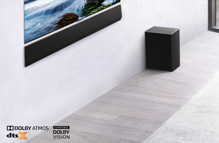 El televisor y la barra de sonido LG están montados en la pared con un subwoofer debajo y a la derecha. La televisión muestra una puesta de sol en el mar.