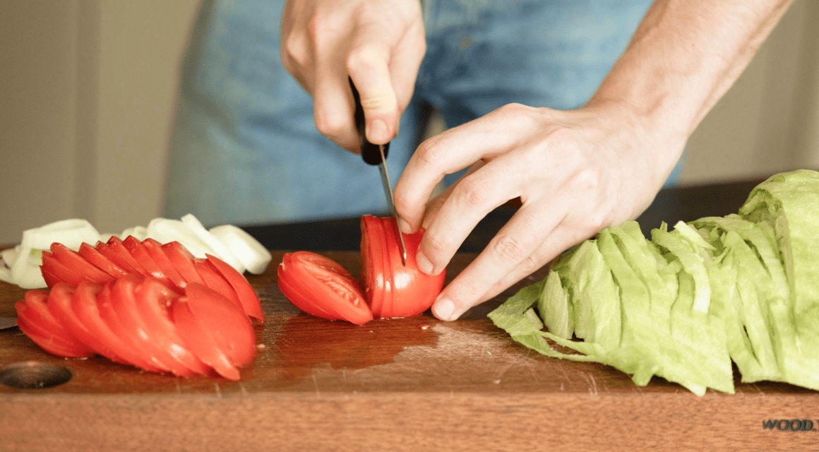 La mano de una mujer cortando tomates y preparándolos para una ensalada.