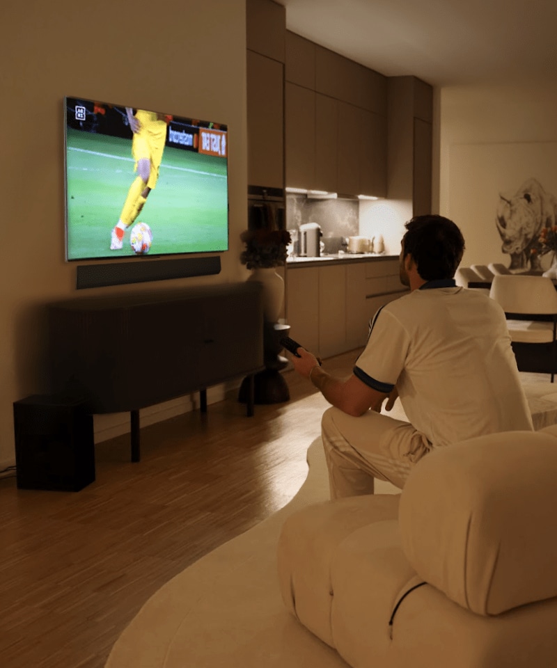 Un hombre sentado en un sofá viendo el LG OLED evo TV en una sala de estar moderna.