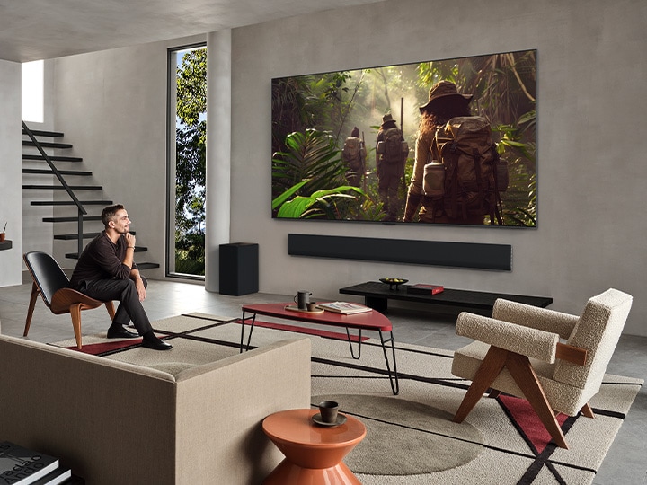 Vista del salón de una lujosa casa. Una pareja está viendo una película en su televisor LG OLED montado en la pared. El dise?o del televisor combina a la perfección con la pared y el estilo del salón.