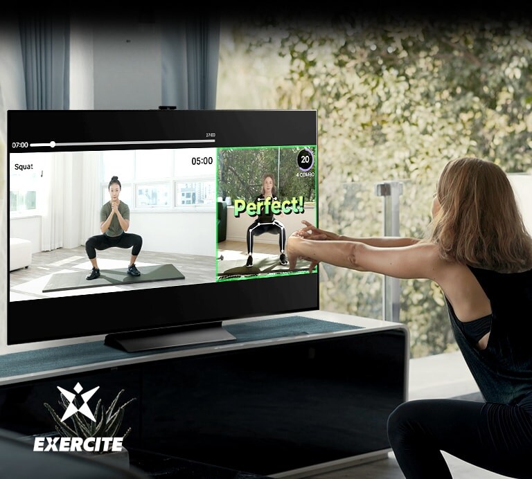 Una mujer está haciendo sentadillas mientras mira el televisor. Dentro de la pantalla, se ven imágenes que ense?an el ejercicio y comprueban tu postura.