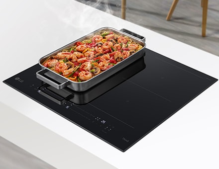 Un large ventilateur est situé sur deux br?leurs de la plaque à induction. Les aliments posés sur la casserole sont en train de fumer.