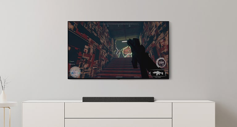 On peut voir un téléviseur et une barre de son dans un salon. Un jeu FPS est diffusé sur un écran de téléviseur et la cha?ne de télévision passe au match de football. (Reproduire la vidéo)