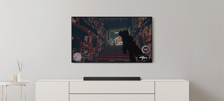 On peut voir un téléviseur et une barre de son dans un salon. Un jeu FPS est diffusé sur un écran de téléviseur et la cha?ne de télévision passe au match de football. (Reproduire la vidéo)