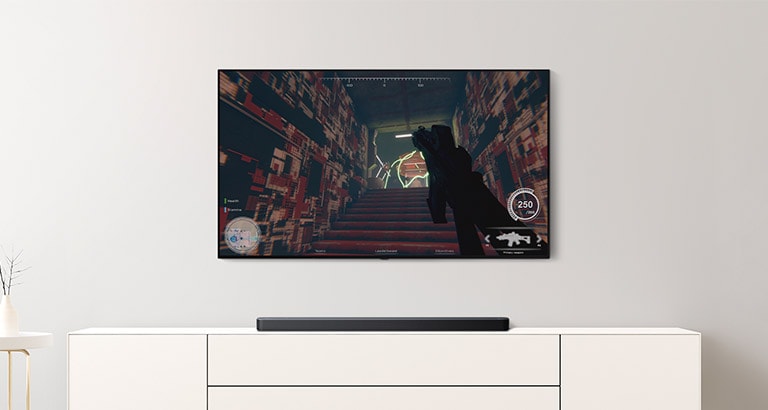 On peut voir un téléviseur et une barre de son dans un salon. Un jeu FPS est diffusé sur un écran de téléviseur et la cha?ne de télévision passe au match de football. (Reproduire la vidéo)