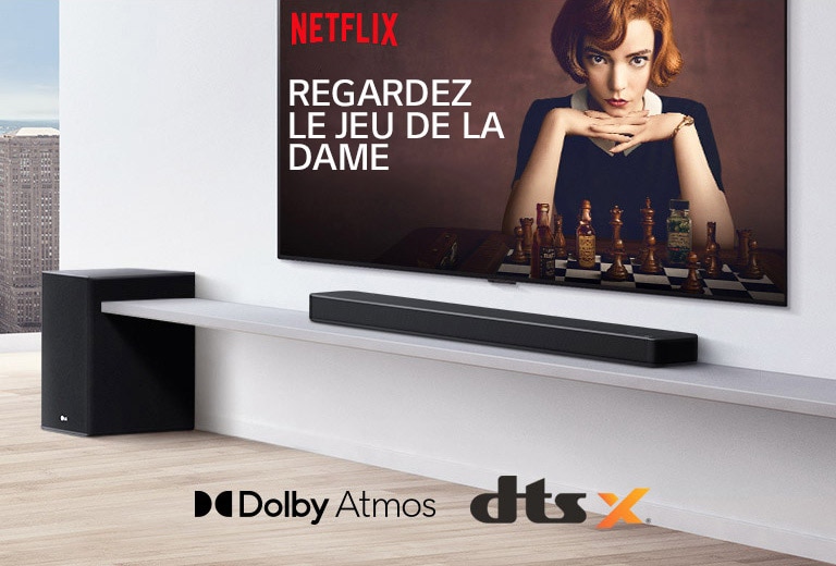 Le téléviseur est fixé au mur. Une affiche d’une émission de télévision est diffusée sur l’écran du téléviseur. La barre de son LG se trouve juste en dessous du téléviseur sur une étagère blanche avec un caisson de basses juste à c?té. Logos Dolby Atmos et DTS: X affichés au milieu en bas de l’image.