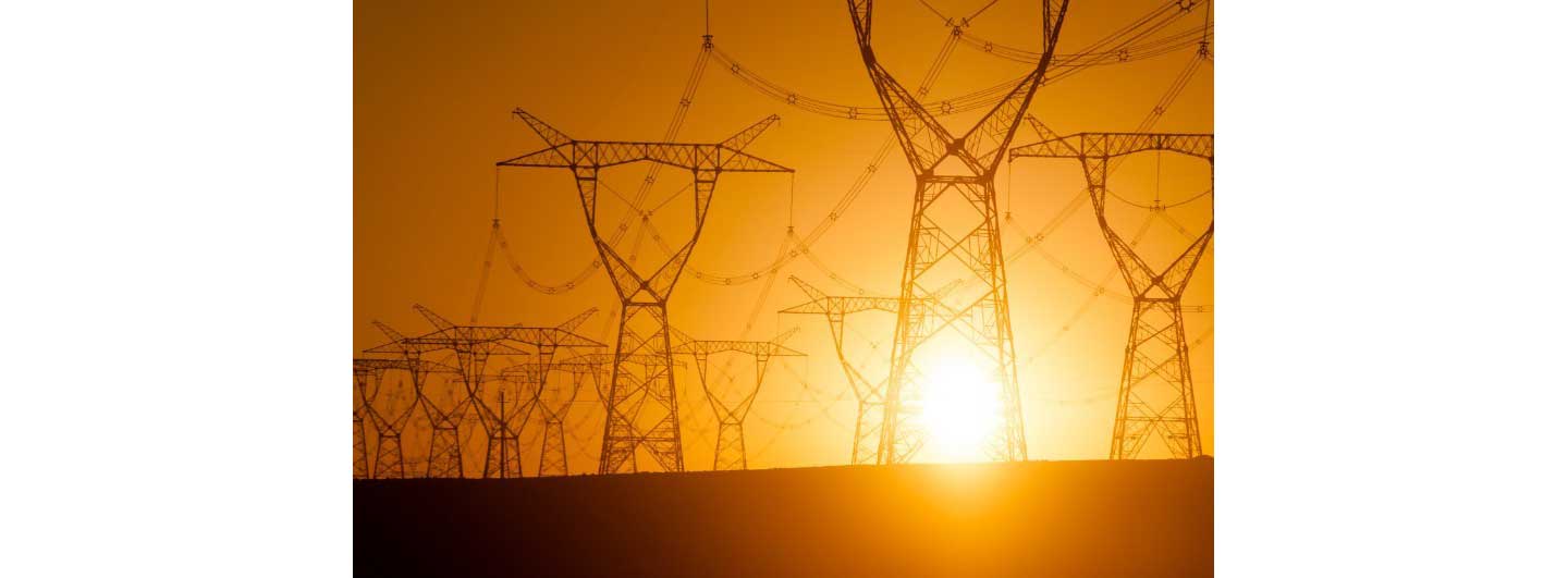 Huge metal power poles and thick wires that transfer the high-voltage electricity in front of the sunset glow