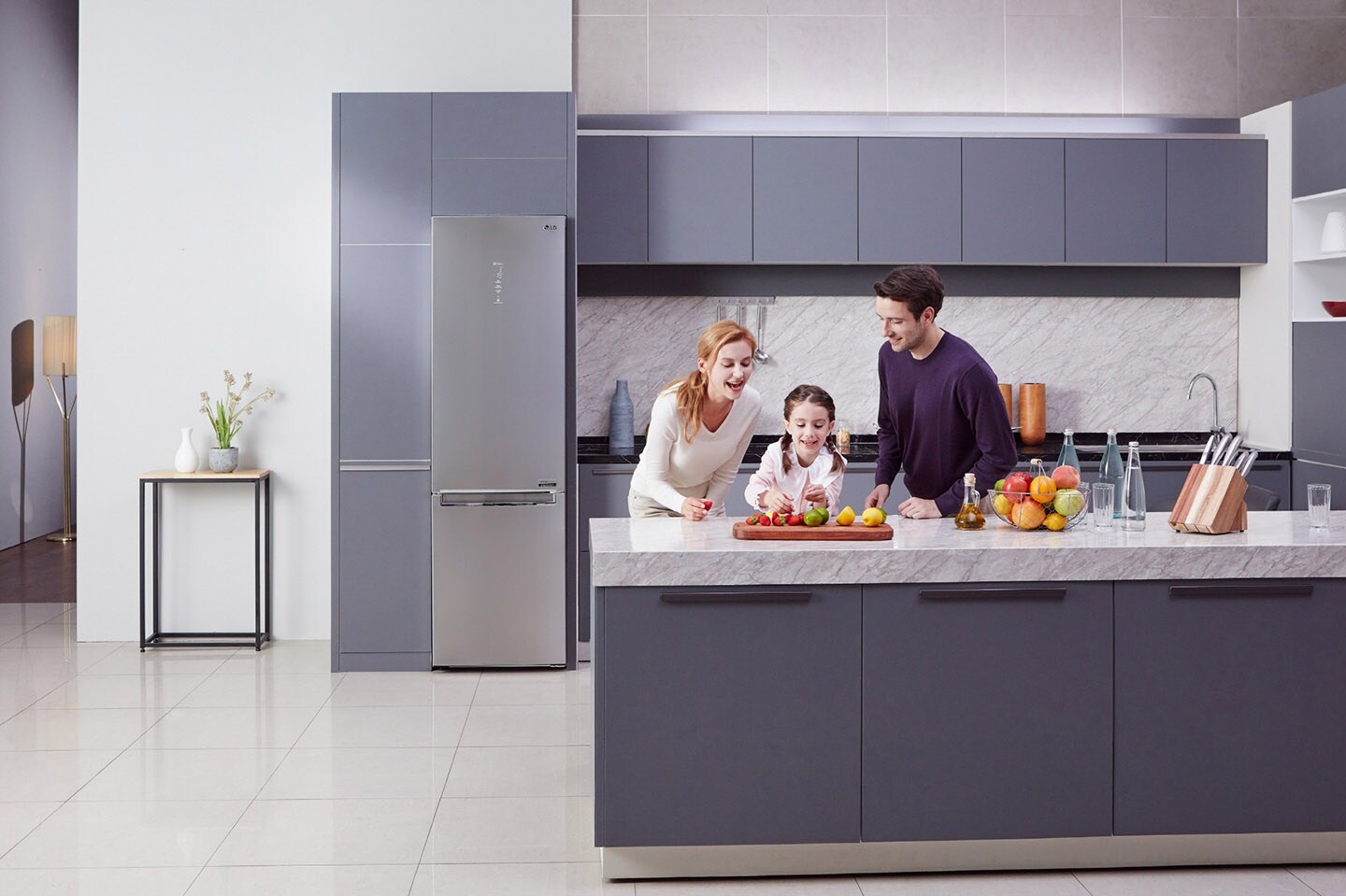Little girl and her parents cutting fruit on the counter with LG Centum System? bottom-freezer refrigerator in the background