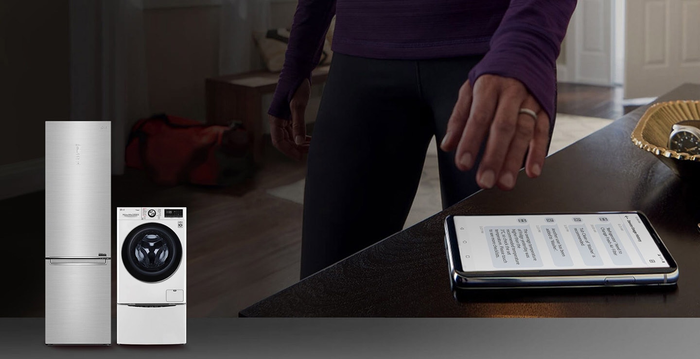 Hand reaching out to a smartphone displaying Device Usage History featuring an LG bottom-freezer refrigerator and TWINWash? washing machine in the lower left corner