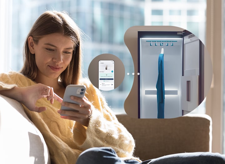 一位女士坐在梳化上使用手機，而 LG Styler 正在運作