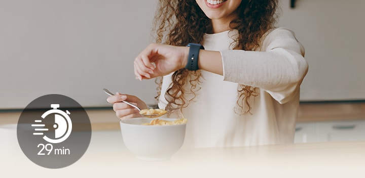 一位女士坐在餐桌旁輕食及看著自己的手錶。一個圖標上面寫著「29 分鐘」。