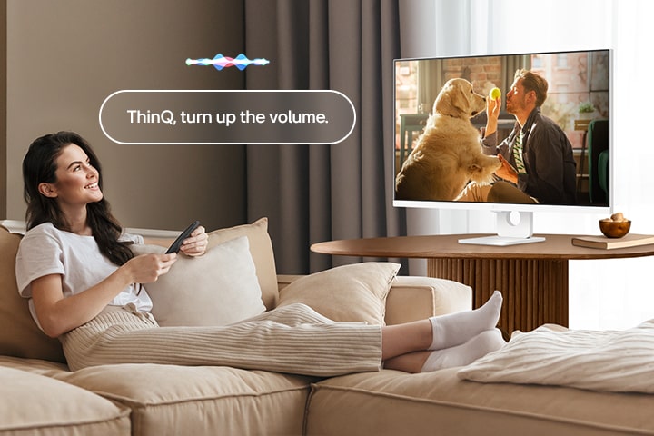 A woman is turning up the LG Smart Monitor’s volume using a Magic Remote.