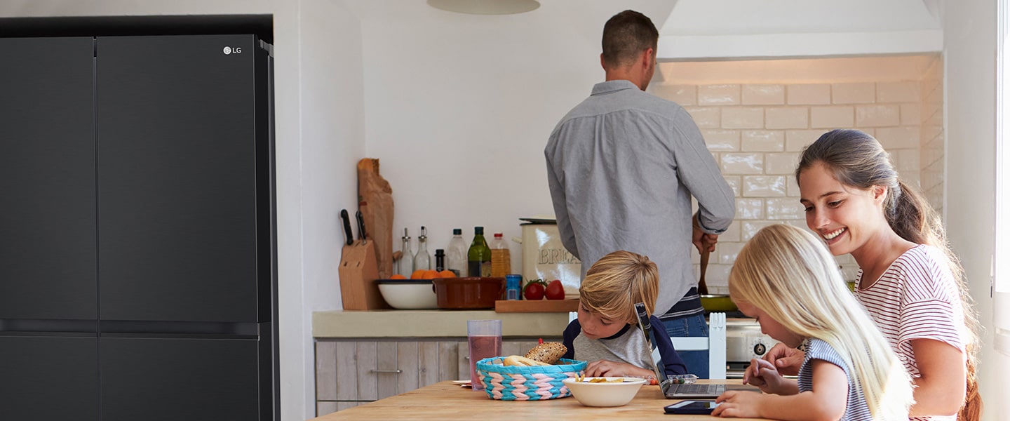 The whole family is sitting at the table preparing a meal. InstaView refrigerator installed on one side of the kitchen is creating cool air quickly.