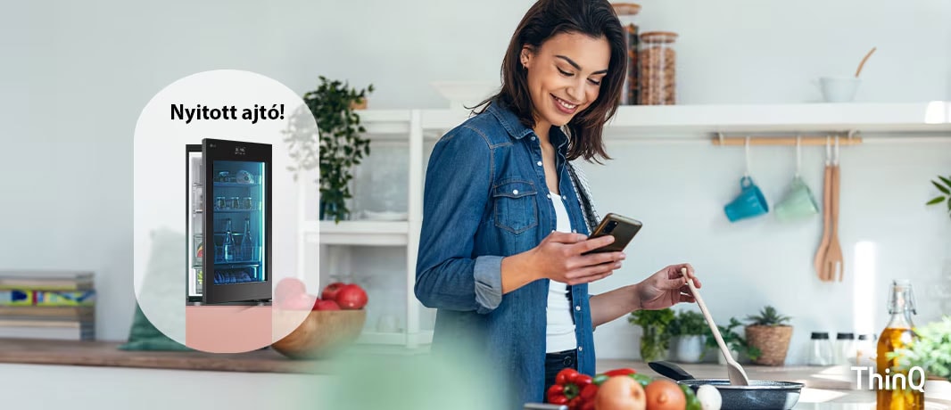 A képen egy n? f?zés k?zben értesítést kap a mobiltelefonjára az LG ThinQ applikációból, a nyitva felejtett h?t? ajtó miatt.