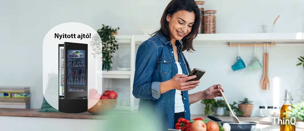 A képen egy n? f?zés k?zben értesítést kap a mobiltelefonjára az LG ThinQ applikációból, a nyitva felejtett h?t? ajtó miatt.