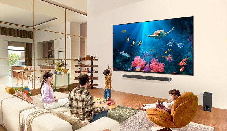 Egy család egy nappaliban, ahol a falra egy ultra nagy LG TV van szerelve, a képerny?jén egy óceáni jelenet korallokkal és tekn?s?kkel.