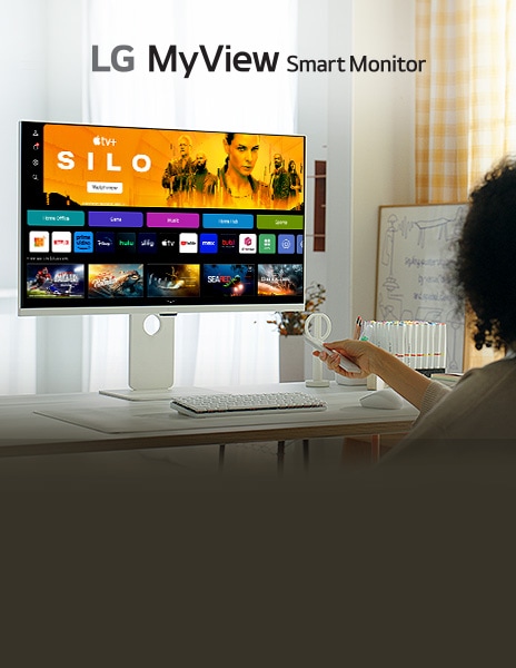 Egy n? okos monitor el?tt ülve az asztalnál a távirányító gombjait nyomkodja.