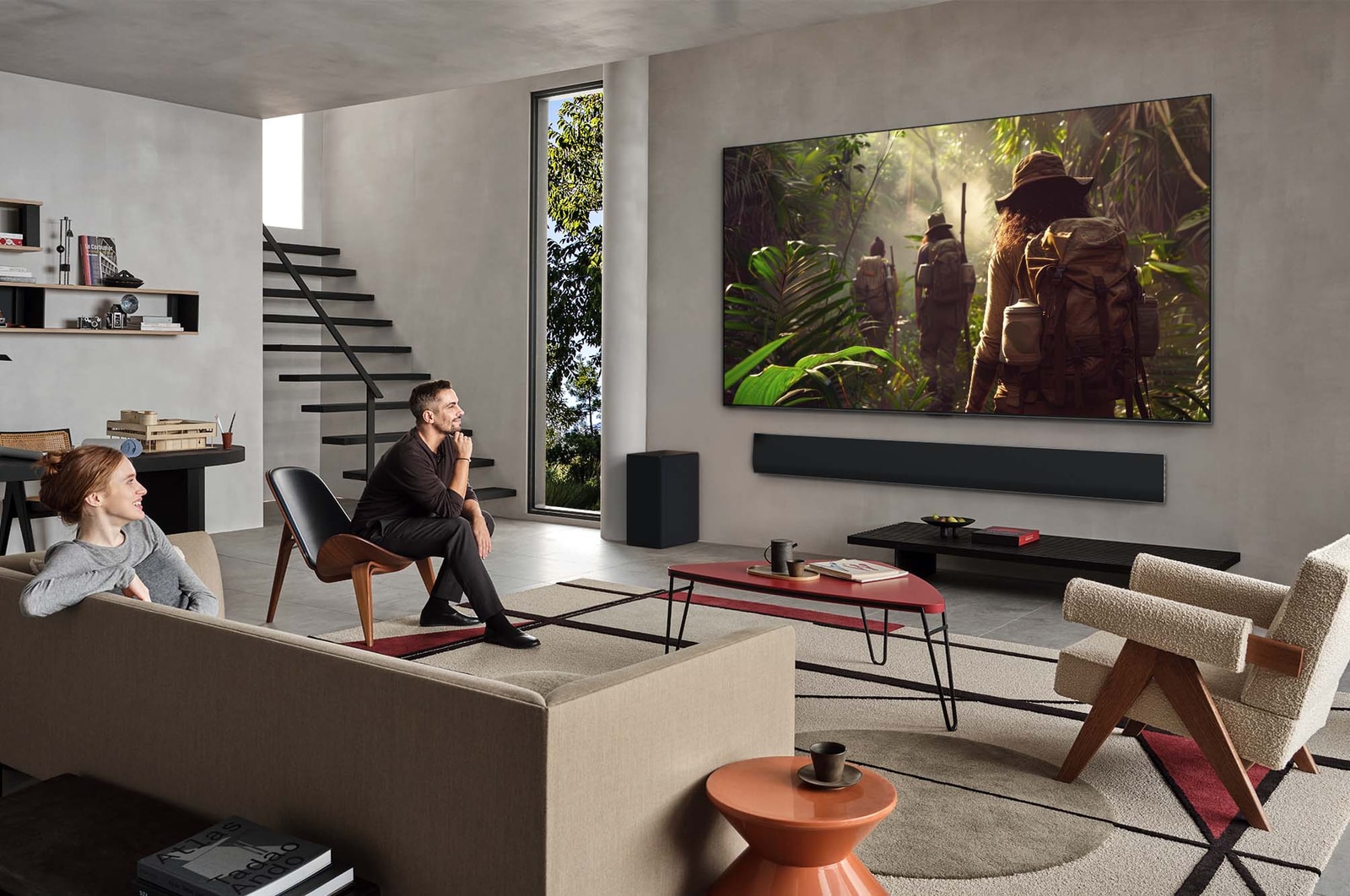 Ampia veduta di un salotto all’interno di una casa prestigiosa, un uomo sta guardando un film sulla LG OLED TV montata sulla parete. Il design del televisore si integra elegantemente con la parete e l’arredamento.