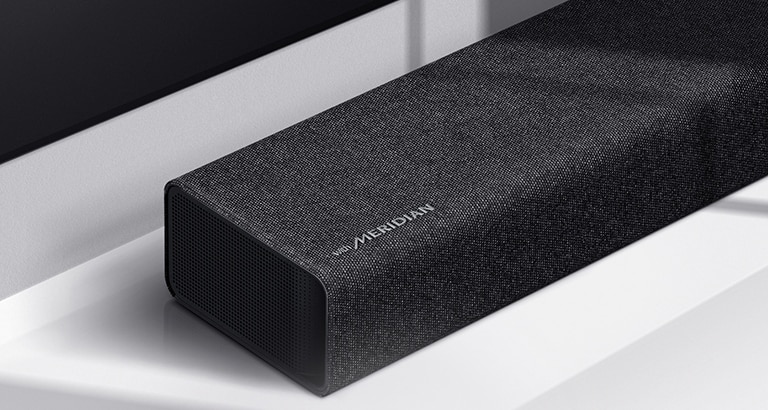 Particolare del lato sinistro della soundbar LG con il logo Meridian in basso a sinistra su un prodotto. è visibile anche il lato inferiore sinistro del televisore.