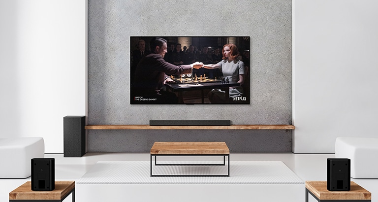 Un set di 2 altoparlanti posteriori, subwoofer e soundbar e un TV collocati in un salotto bianco. Sullo schermo del TV si vede il poster di uno show televisivo.
