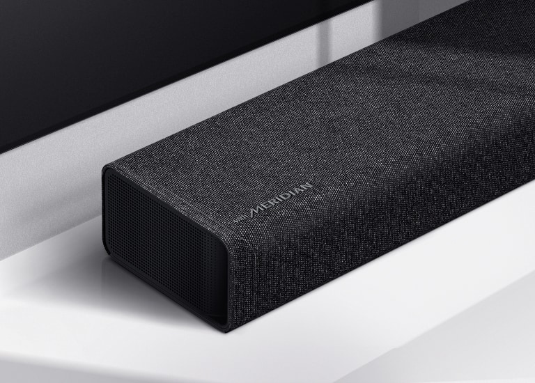 Particolare del lato sinistro della soundbar LG con il logo Meridian in basso a sinistra su un prodotto. è visibile anche il lato inferiore sinistro del televisore.