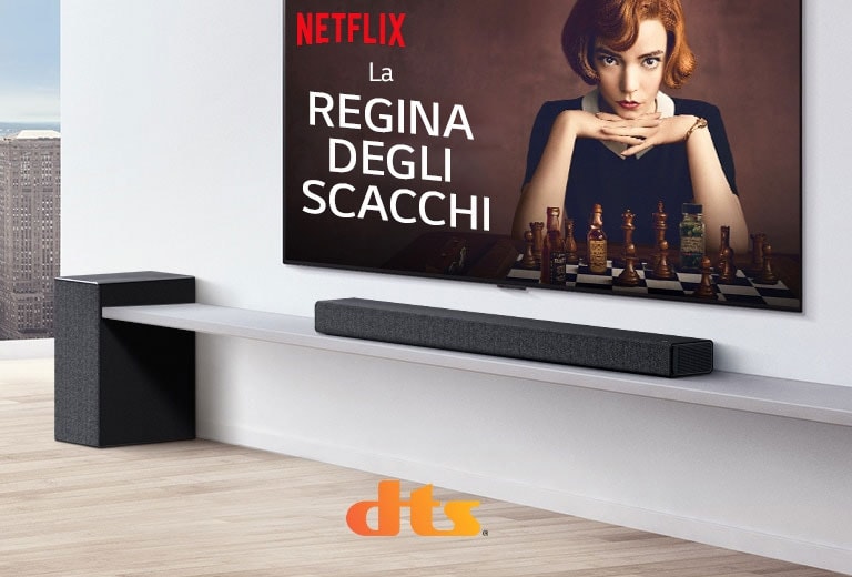Il televisore è sulla parete.  Sullo schermo del TV vediamo il poster di una serie TV. La Soundbar LG è appena sotto al TV, su una mensola bianca, con un subwoofer a fianco. I loghi di Dolby Atmos e DTS:X sono visualizzati sulla parte inferiore centrale dell’immagine.