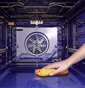   Una mano pulisce il fondo di un forno con un panno giallo, mostrando il sistema di ventilazione sulla parete posteriore.