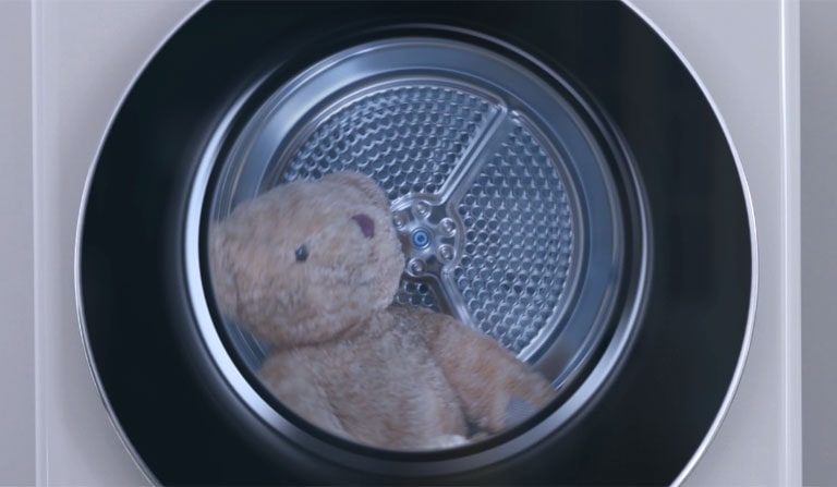 Un orsacchiotto di peluche gira all'interno di un'asciugatrice LG in funzione.