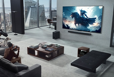 壁掛けのLGトゥルーワイヤレスTVとLG Soundbarでビデオゲームをしている人がいるリビングルーム。手にコントローラを握りっているが、ゲーミングコンソールはすぐに見えない。これらも目に見える配線がありません。Zero Connect Boxがサイドテーブルの下にしまわれ、ほとんど見えない。