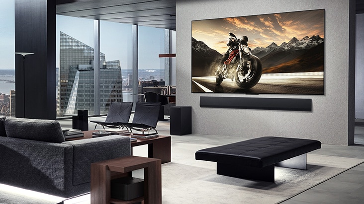 LG OLED M4 et LG Soundbar installées sur le mur du salon d’un appartement en hauteur. La disposition est sans encombrement. Le bo?tier Zero Connect peut être vu, caché sous une table d’appoint près d’un canapé.