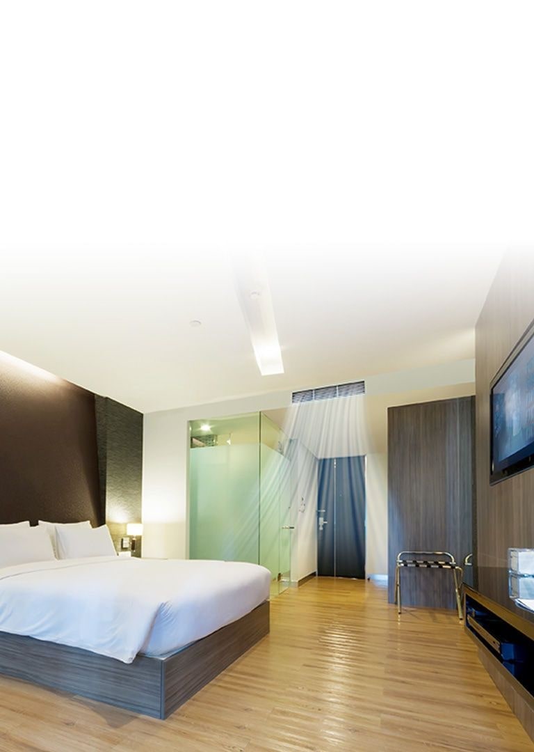 Un Ducto oculto en Plafón suministra corriente de aire de color azul en una habitación de hotel con paredes de tonos cafés y una cama tama?o queen cubierta con sábanas blancas.