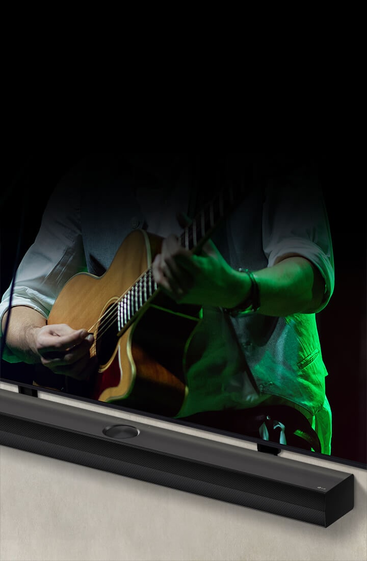 La barra de sonido LG sobre un fondo negro revela su dise?o comenzando desde la esquina izquierda y luego se amplía para mostrar toda la barra de sonido. Aparece un televisor LG QNED con soporte Synergy. La barra de sonido se encuentra sobre el soporte Synergy, presiona contra la pared y la pantalla inferior del televisor es visible, mostrando a un hombre tocando la guitarra.