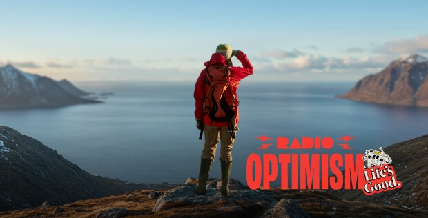 A woman wearing a red hiking jacket is standing in a place where the vast ocean and snow-covered mountains can be seen. The image also features the "Radio Optimism" slogan logo and the "Life's Good." logo alongside the woman.
