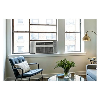 Window air conditioner installed in a living room with a sofa and plants