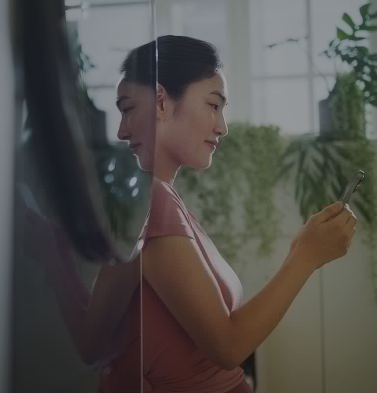 La imagen muestra a una mujer de pie junto a una torre de lavado LG WashTower?, mirando su teléfono mientras sonríe.
