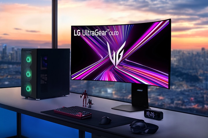 LG UltraGear OLED-monitor op een gamebureau met pc-opstelling, met uitzicht op een stadsgezicht bij zonsondergang.