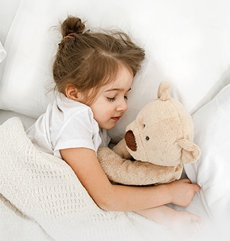 Una ni?a está tumbada en la cama con una mu?eca en brazos