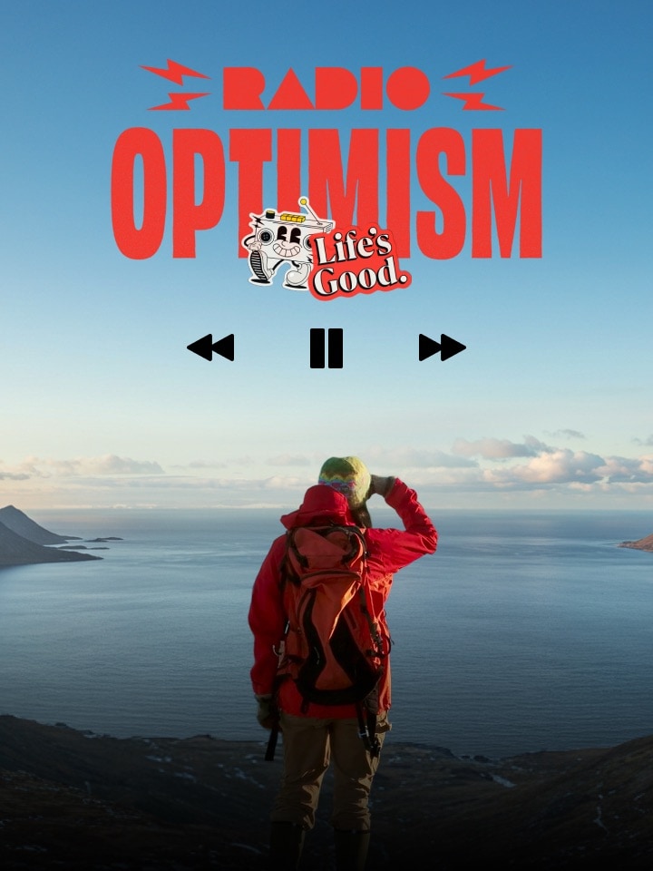 A woman wearing a red hiking jacket is standing in a place where the vast ocean and snow-covered mountains can be seen.