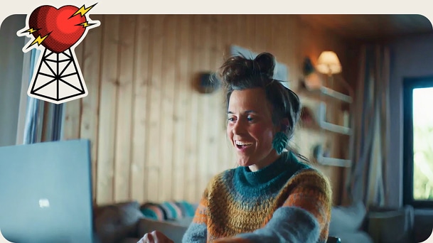 A woman smiles brightly as she looks at her laptop in a spacious room.