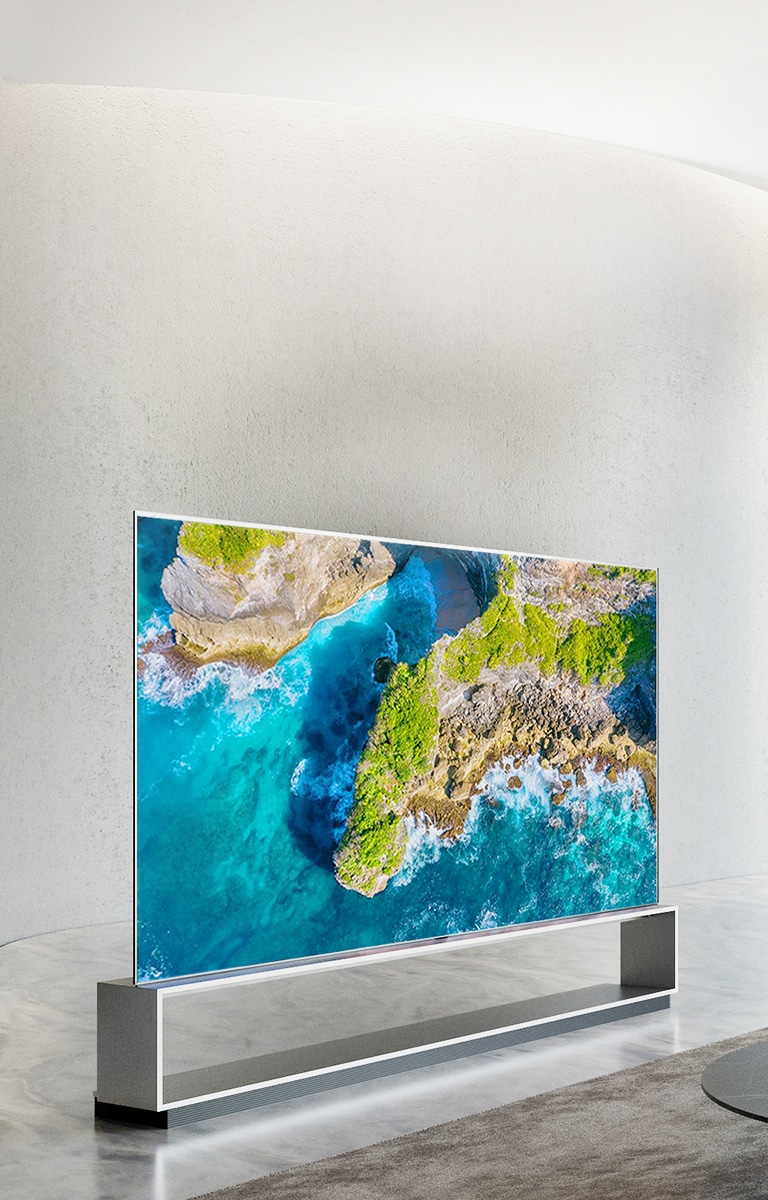 Telewizor LG SIGNATURE OLED W9 jest zawieszony na ?cianie, a przed telewizorem le?y kranik z niebieskim niebem nad oknem.
