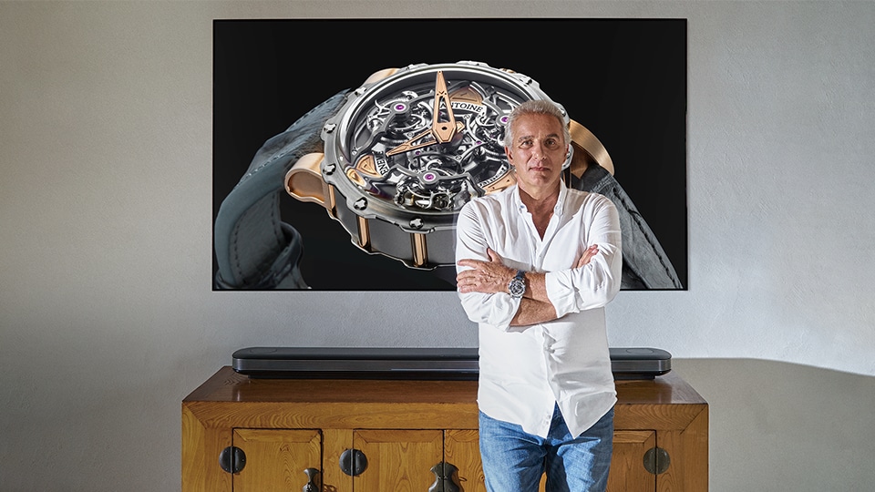 Zegarmistrz Antoine Preziuso stoi przed telewizorem LG SIGNATURE OLED W.